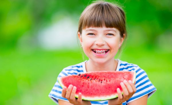 Child eating watermelon. Kids eat fruits in the garden. Pre teen girl in the garden holding a slice of water melon. happy girl kid eating watermelon. Girl kid with gasses and teeth braces.